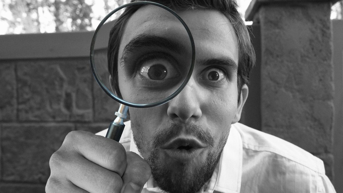 Person looking through a magnifying glass, showing an expression of awe and discovery, symbolizing in-depth analysis and revelation.