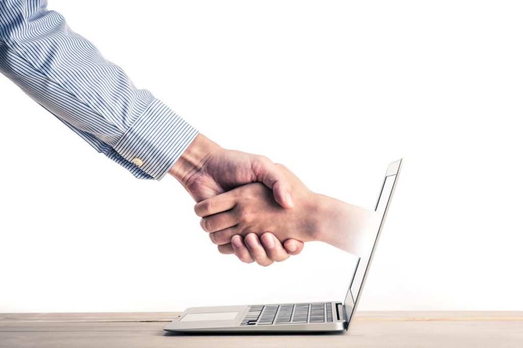 Handshake coming out of a laptop screen, merging technology and personal connection.