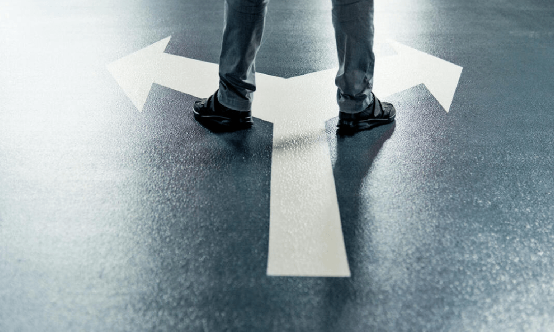 Man standing at a crossroads, looking thoughtfully at two diverging paths, symbolizing a crucial decision-making moment.