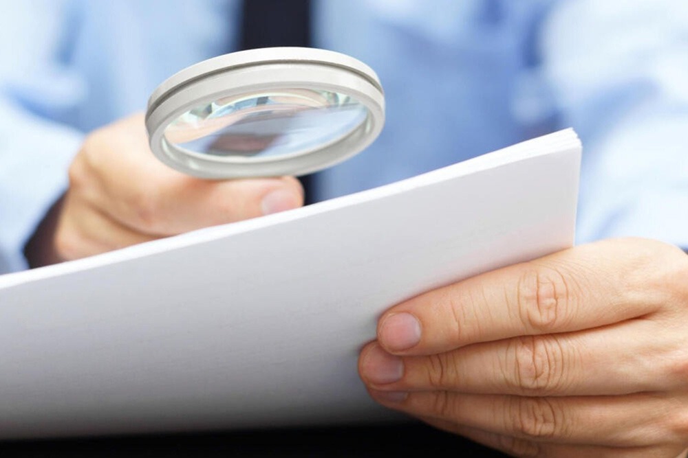 A professional scrutinizing documents with a magnifying glass.